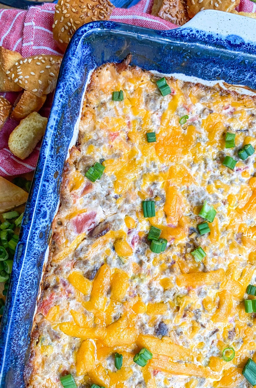 bacon cheeseburger dip in a blue baking dish surrounded by hamburger bun croutons