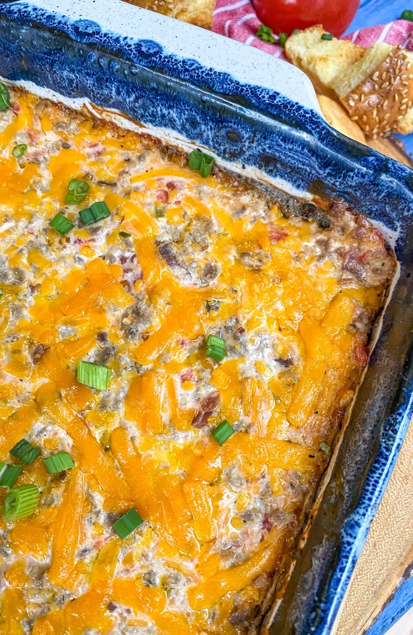 bacon cheeseburger dip in a blue baking dish surrounded by hamburger bun croutons