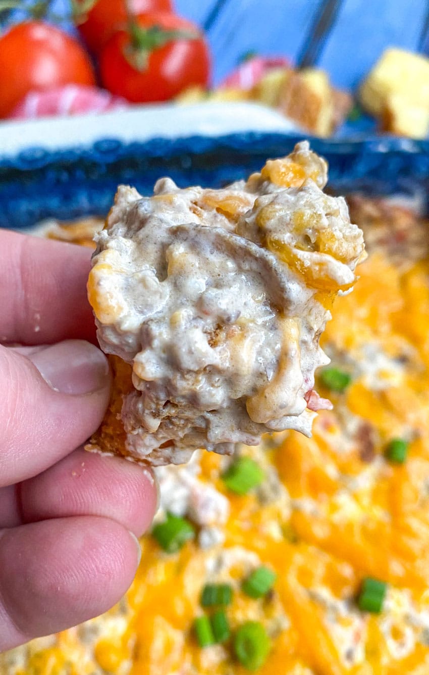 a hand holding up a hamburger bun crouton topped with creamy cheeseburger dip