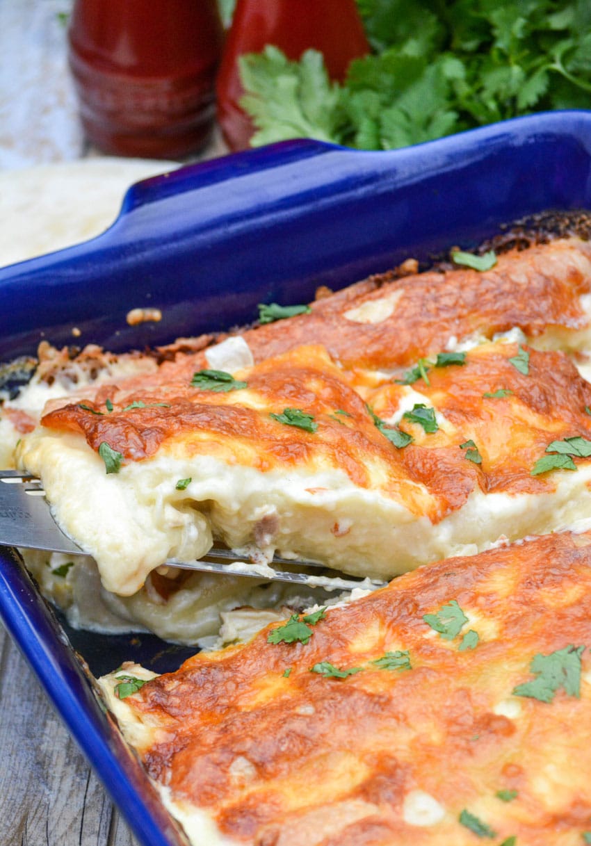 a spatula lifting a creamy white chicken enchilada out of a blue baking dish