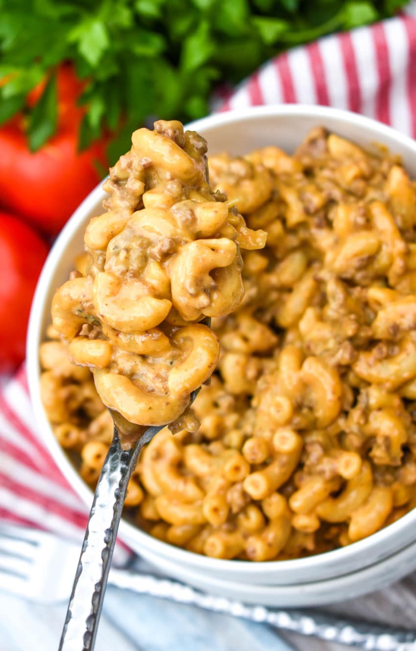 a fork holding up a scoop of extra creamy hamburger helper from scratch over a white bowl