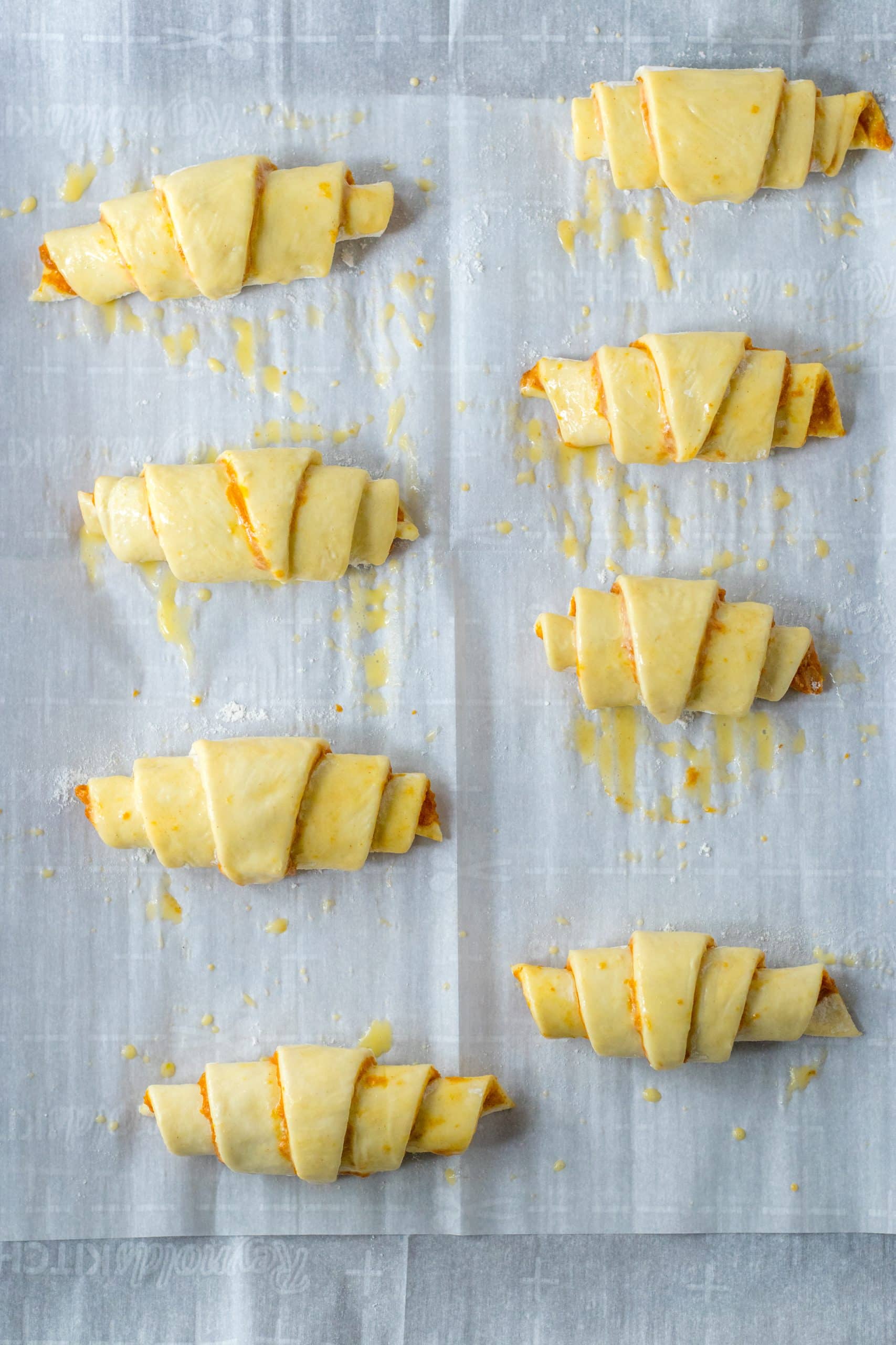unbaked pumpkin pie crescent rolls basted with egg wash on a parchment paper lined baking sheet