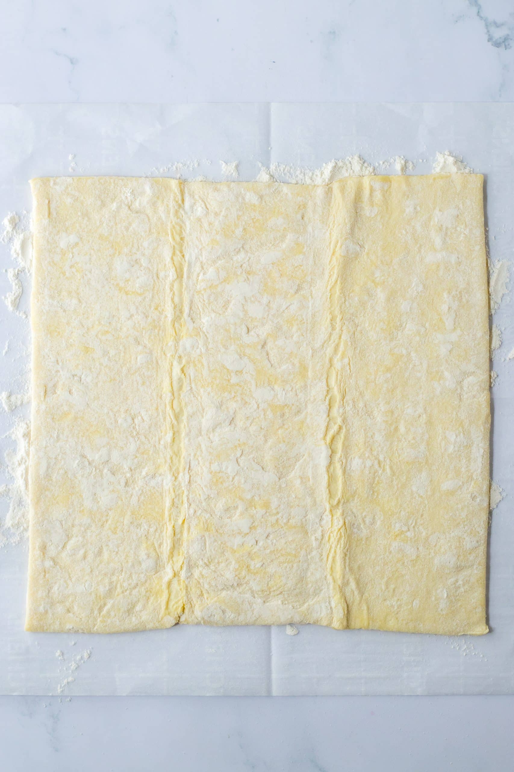 unrolled flattened sheet of puff pastry on a floured countertop