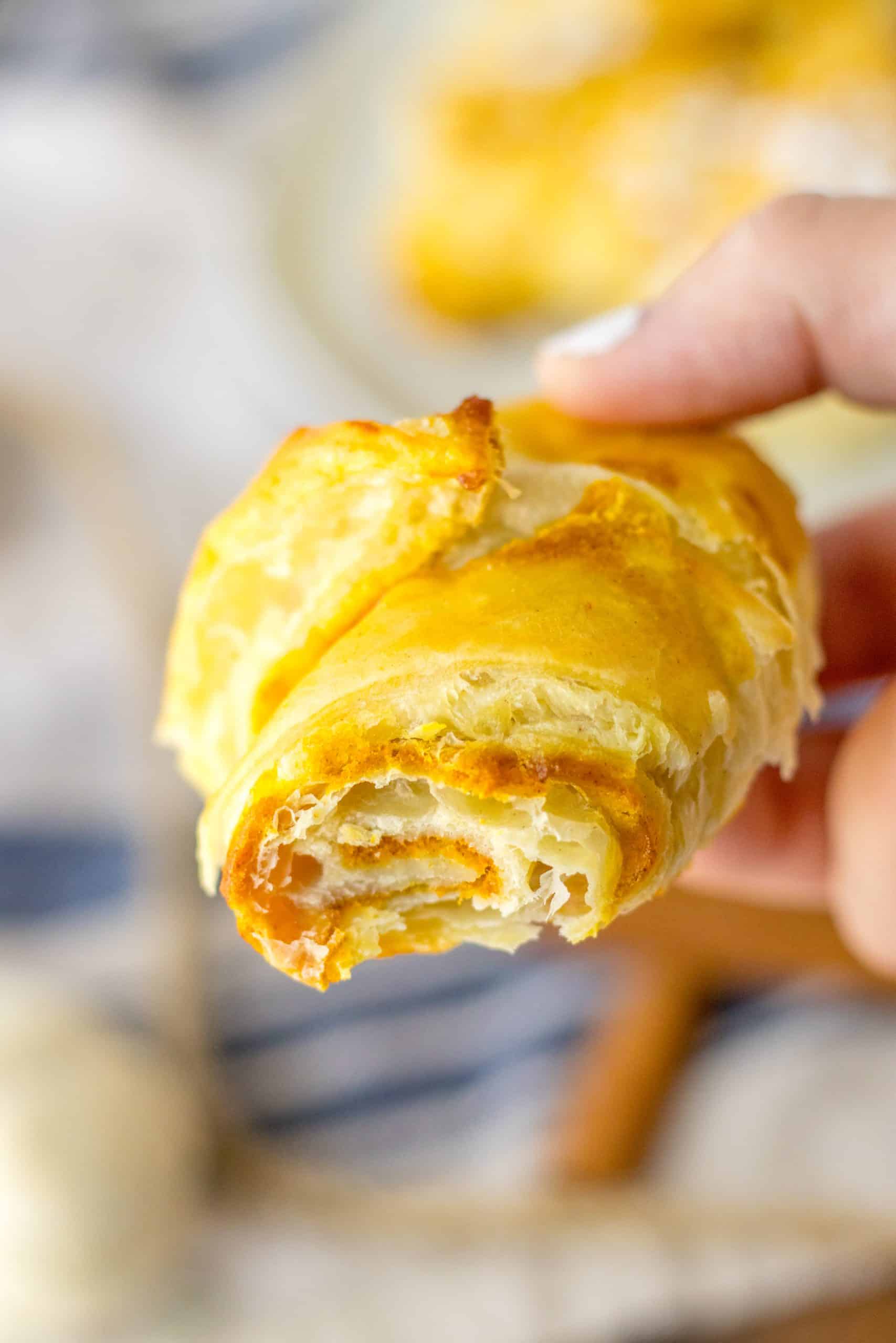 a hand holding up a bitten pumpkin pie crescent roll