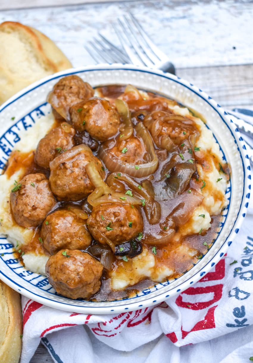 crockpot meatballs with onions and gravy over mashed potatoes in a blue and white bowl