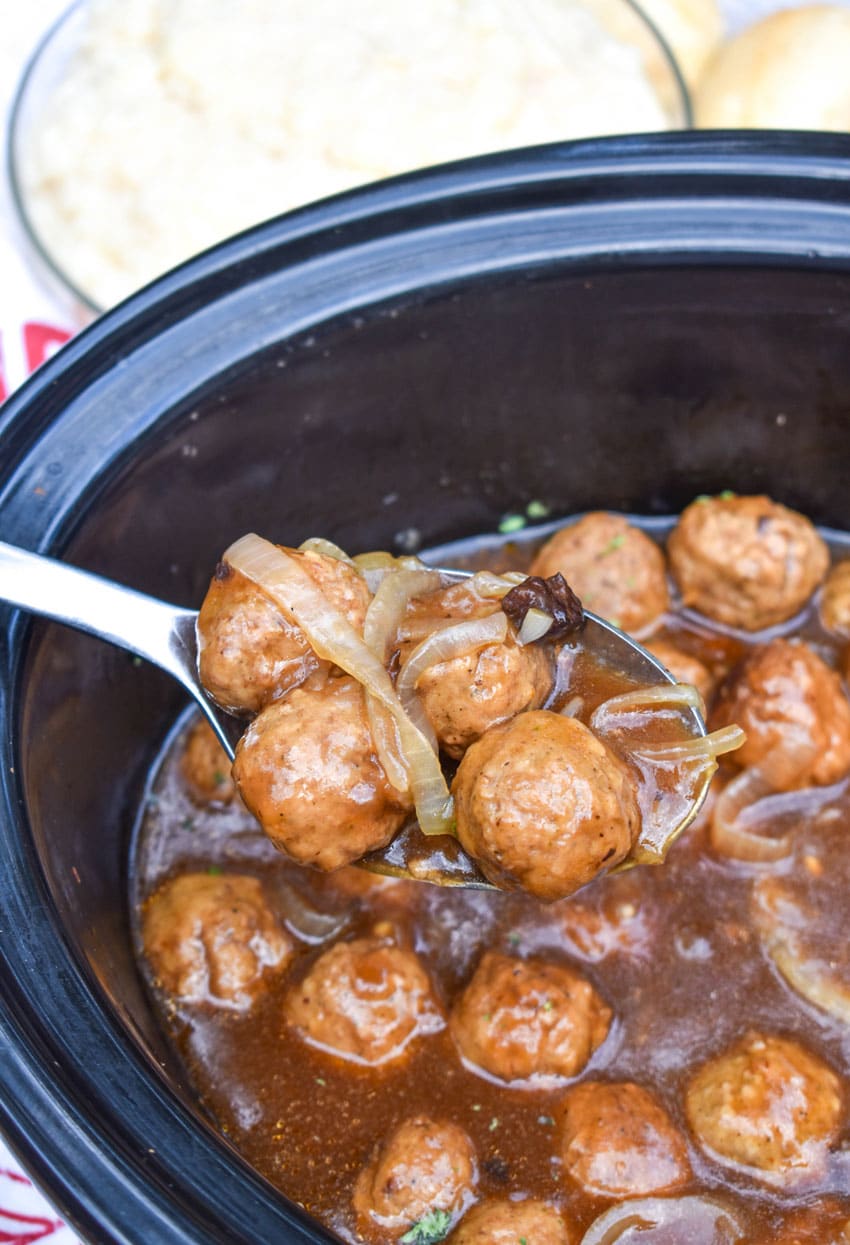 a silver spoon in a black crockpot filled with slow cooker salisbury steak meatballs