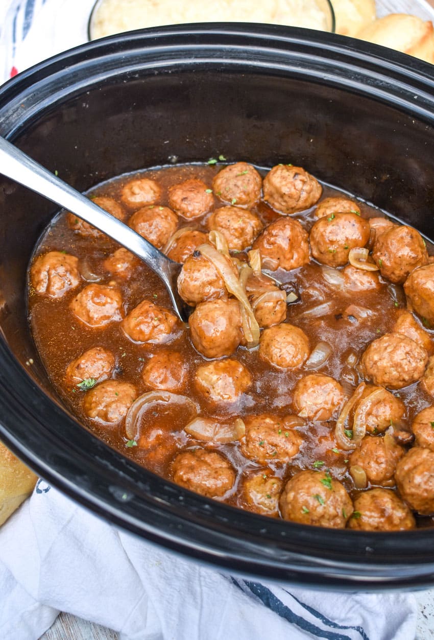 a silver spoon in a black crockpot filled with slow cooker salisbury steak meatballs