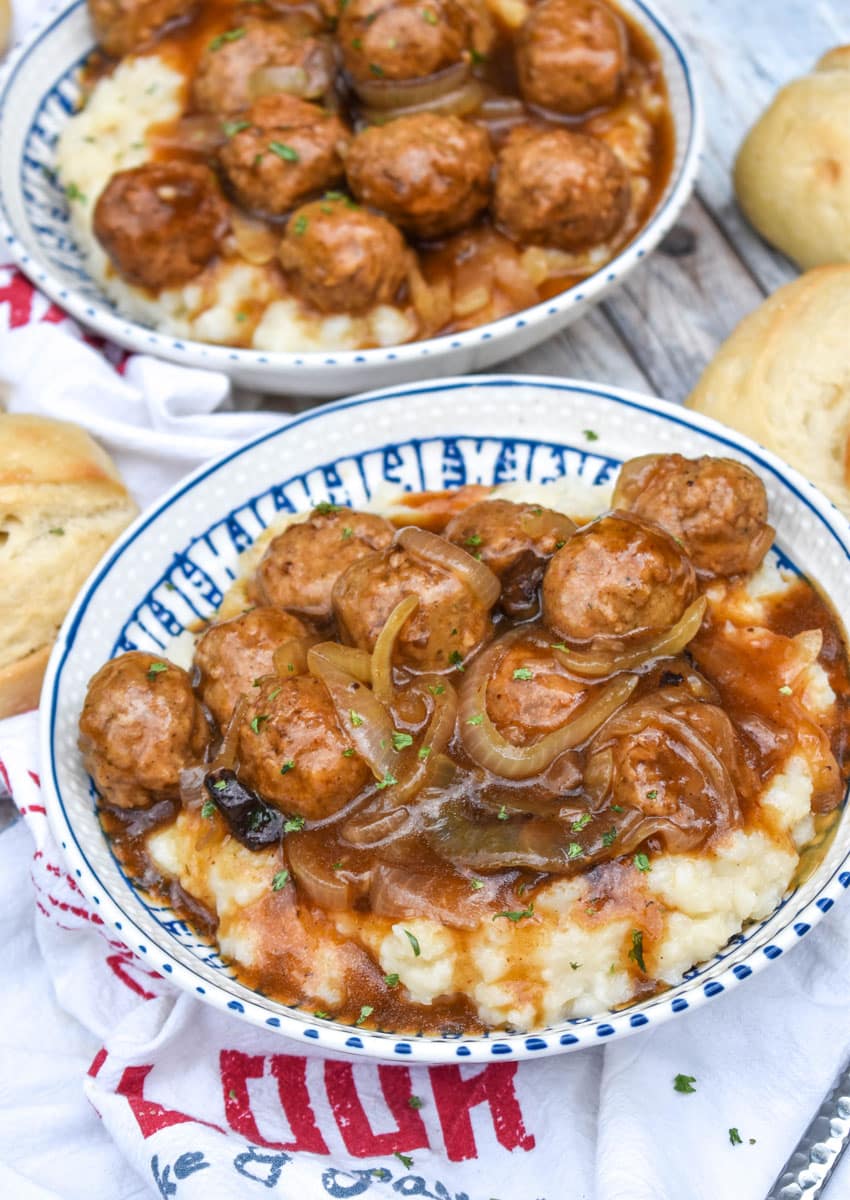 salisbury steak meatballs in gravy over mashed potatoes in two blue and white bowls