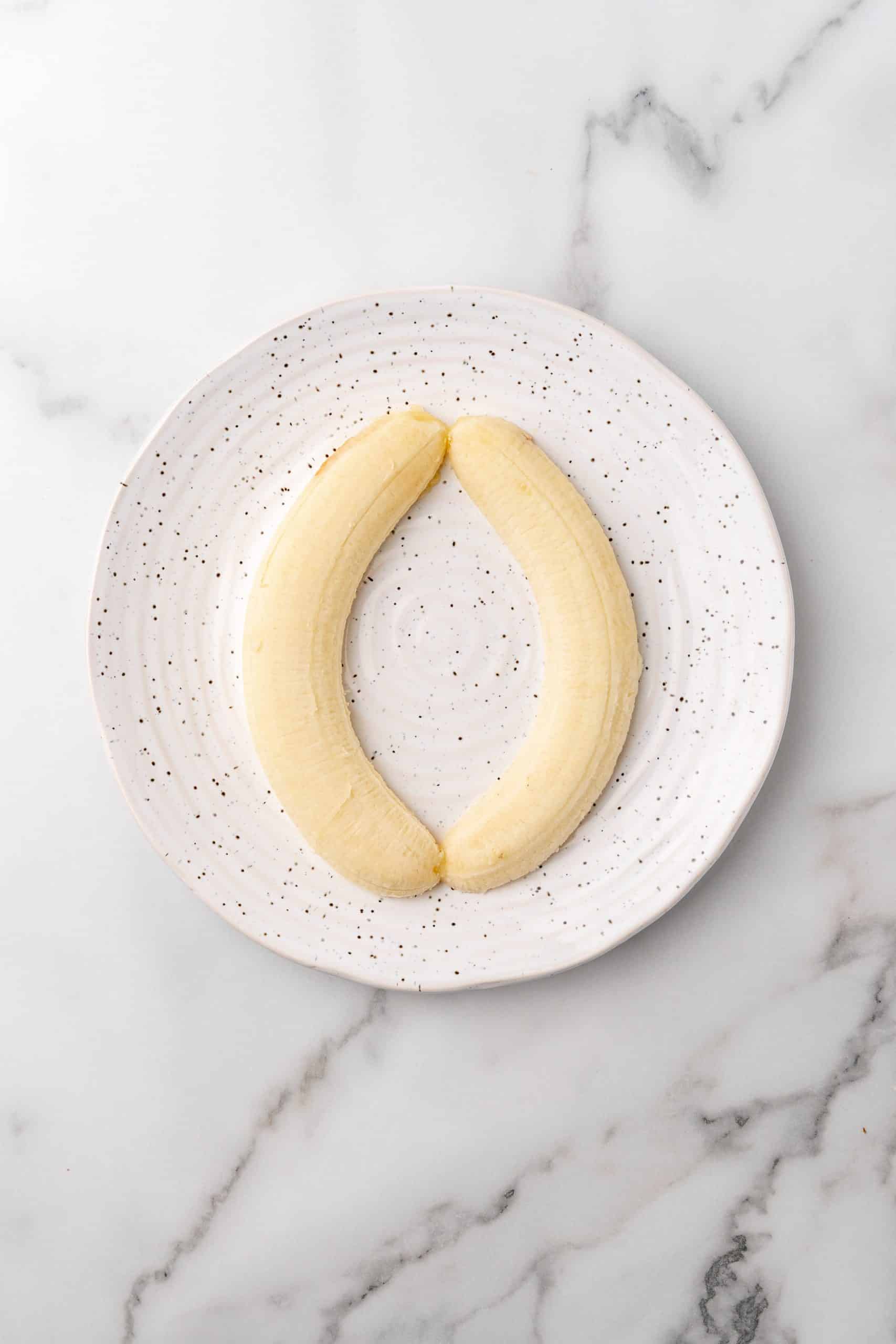 two halves of a banana on a speckled white plate