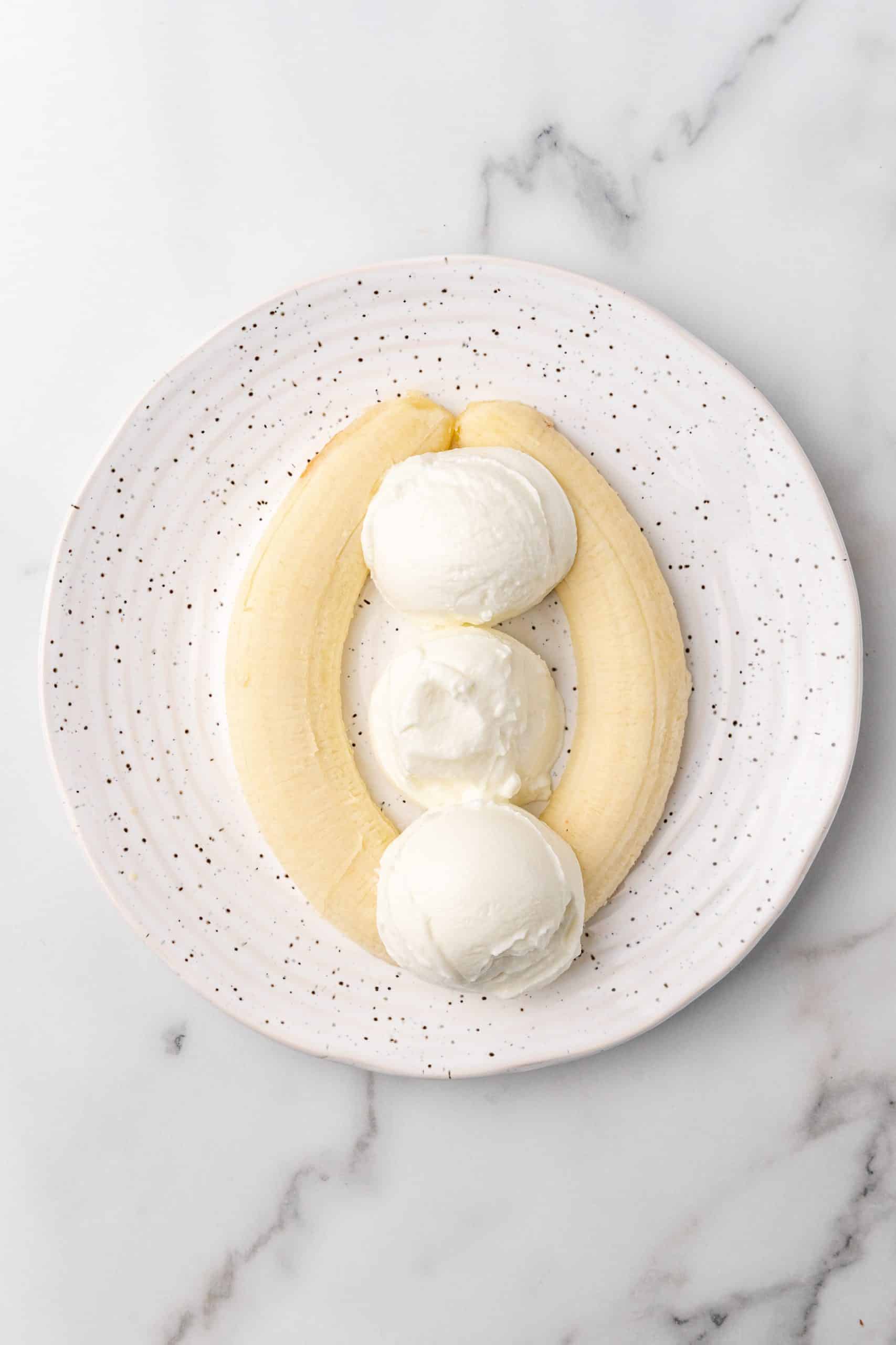 three scoops of greek yogurt in between two sliced bananas on a white speckled plate