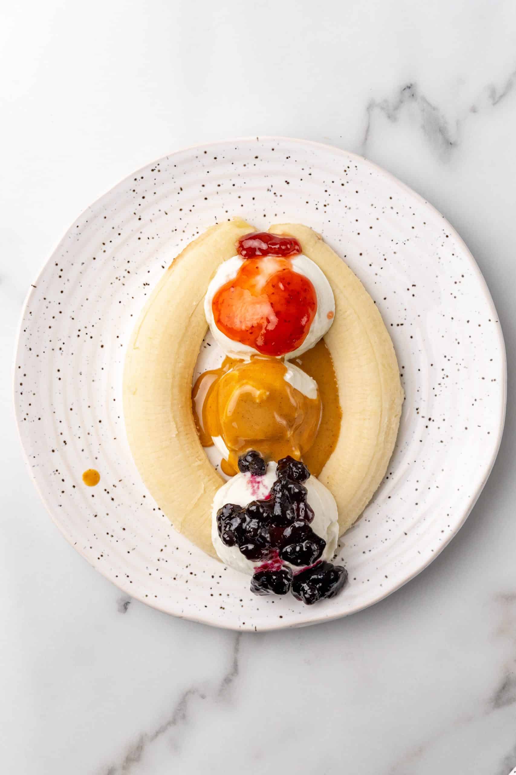 different jams over top scoops of greek yogurt and sliced bananas on a speckled white plate