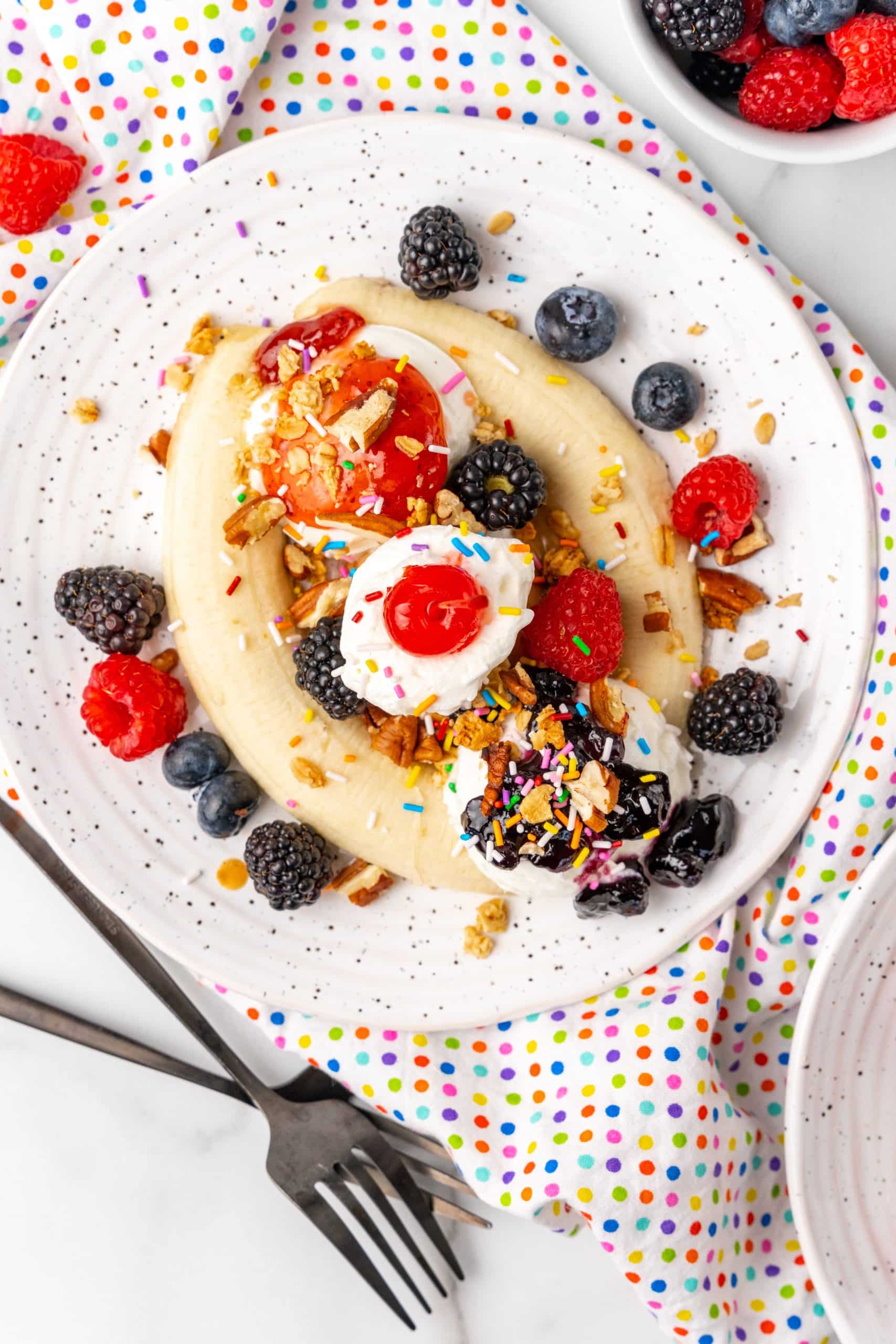 a breakfast banana split on a white speckled plate with nuts and fresh berries