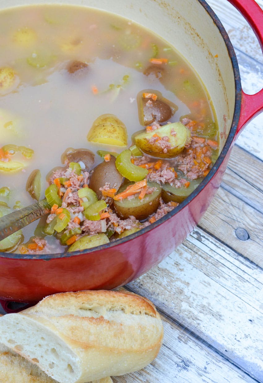 a silver ladle scooping canned corned beef stew out of a red dutch oven