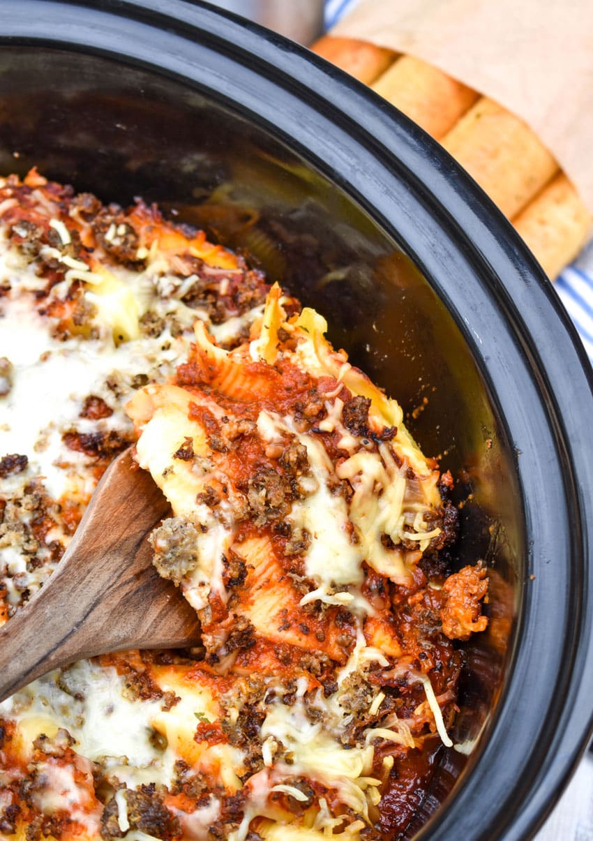 a wooden spatula scooping slow cooker stuffed shells out of a black crock