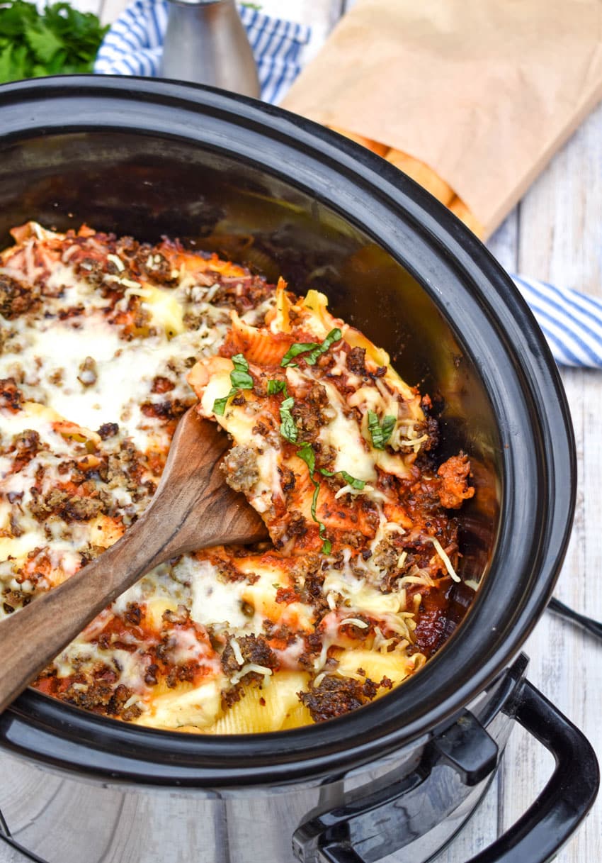 a wooden spatula scooping slow cooker stuffed shells out of a black crock