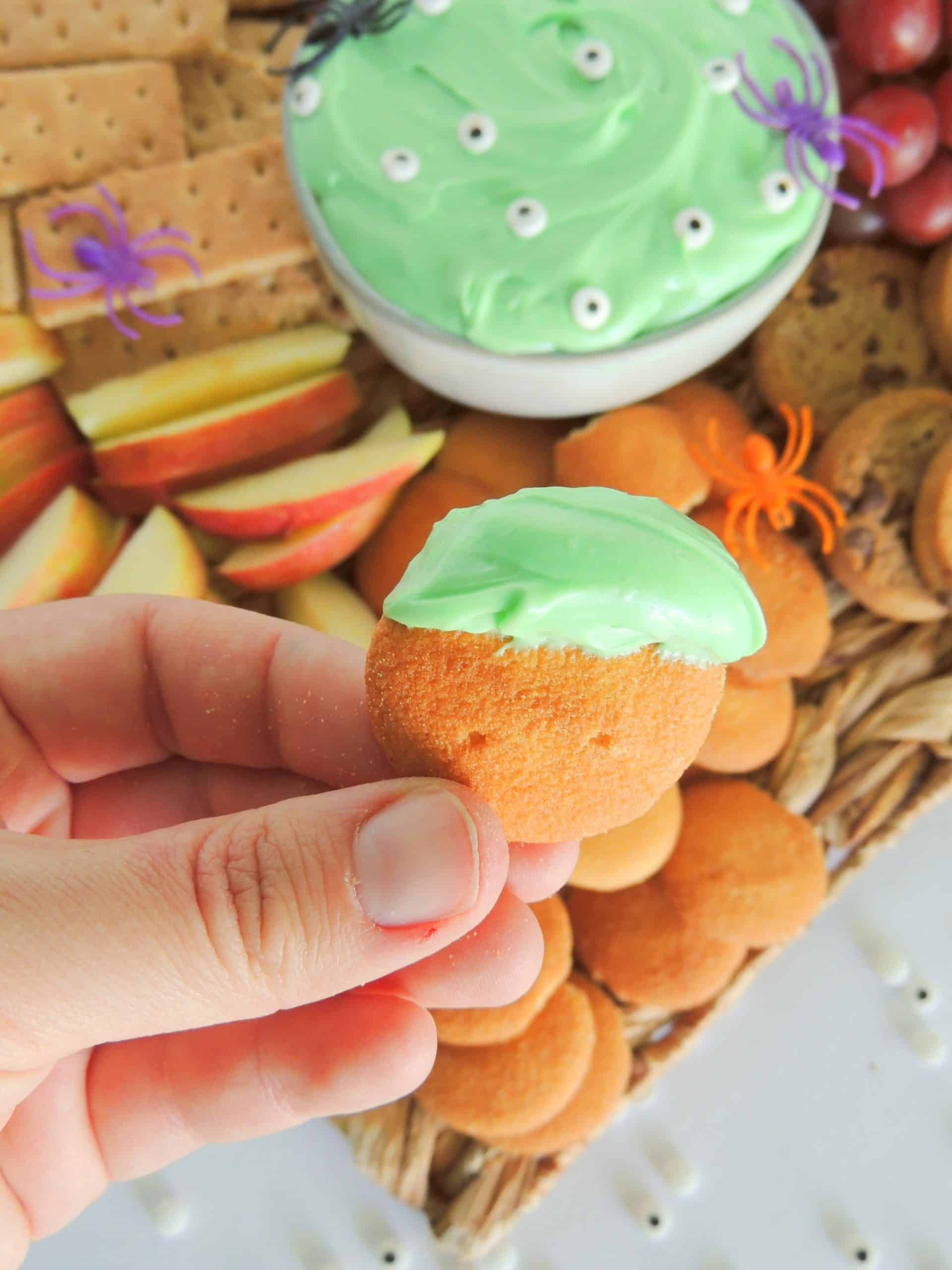 a hand holding up a nilla wafer topped with spooky halloween dip