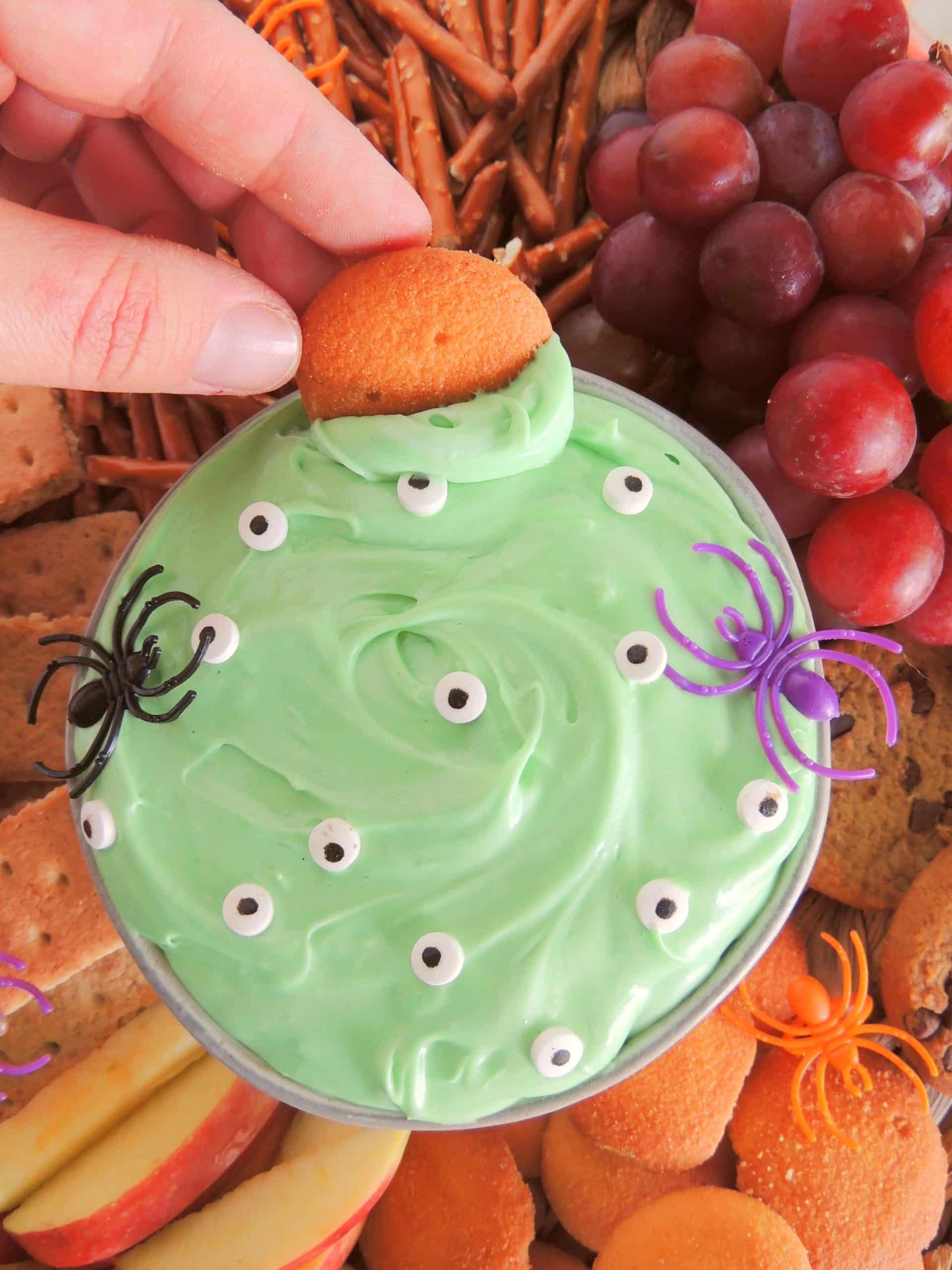 a hand dunking a nilla wafer in a bowl of spooky halloween dip