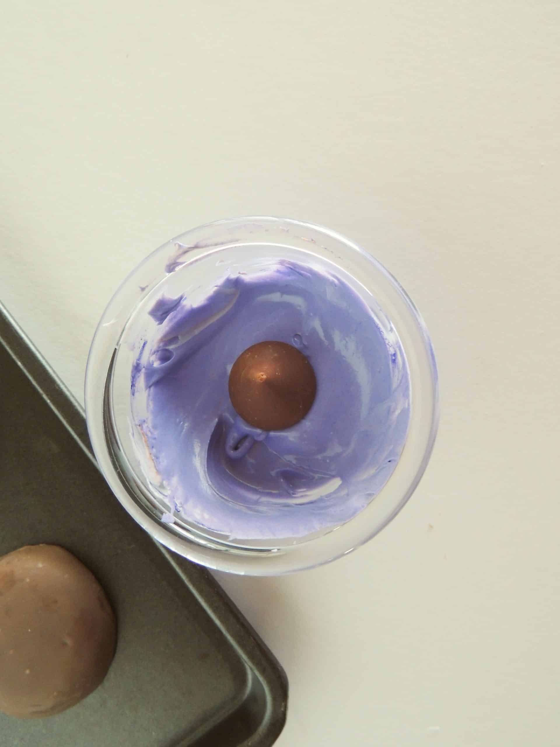 an unwrapped hershey kiss sitting in a small bowl of melted purple chocolate