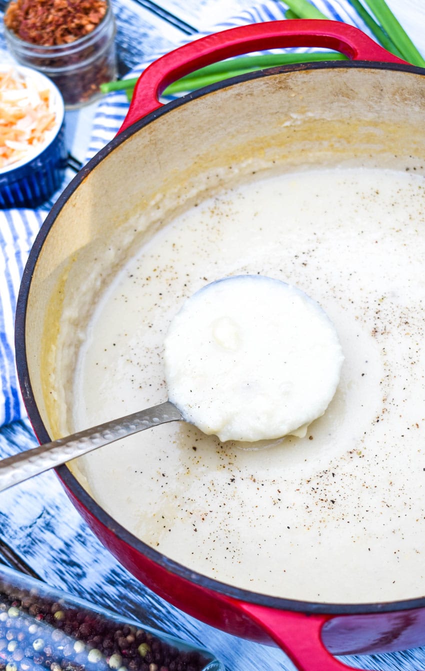 a silver ladle scooping leftover mashed potato soup out of a large dutch oven