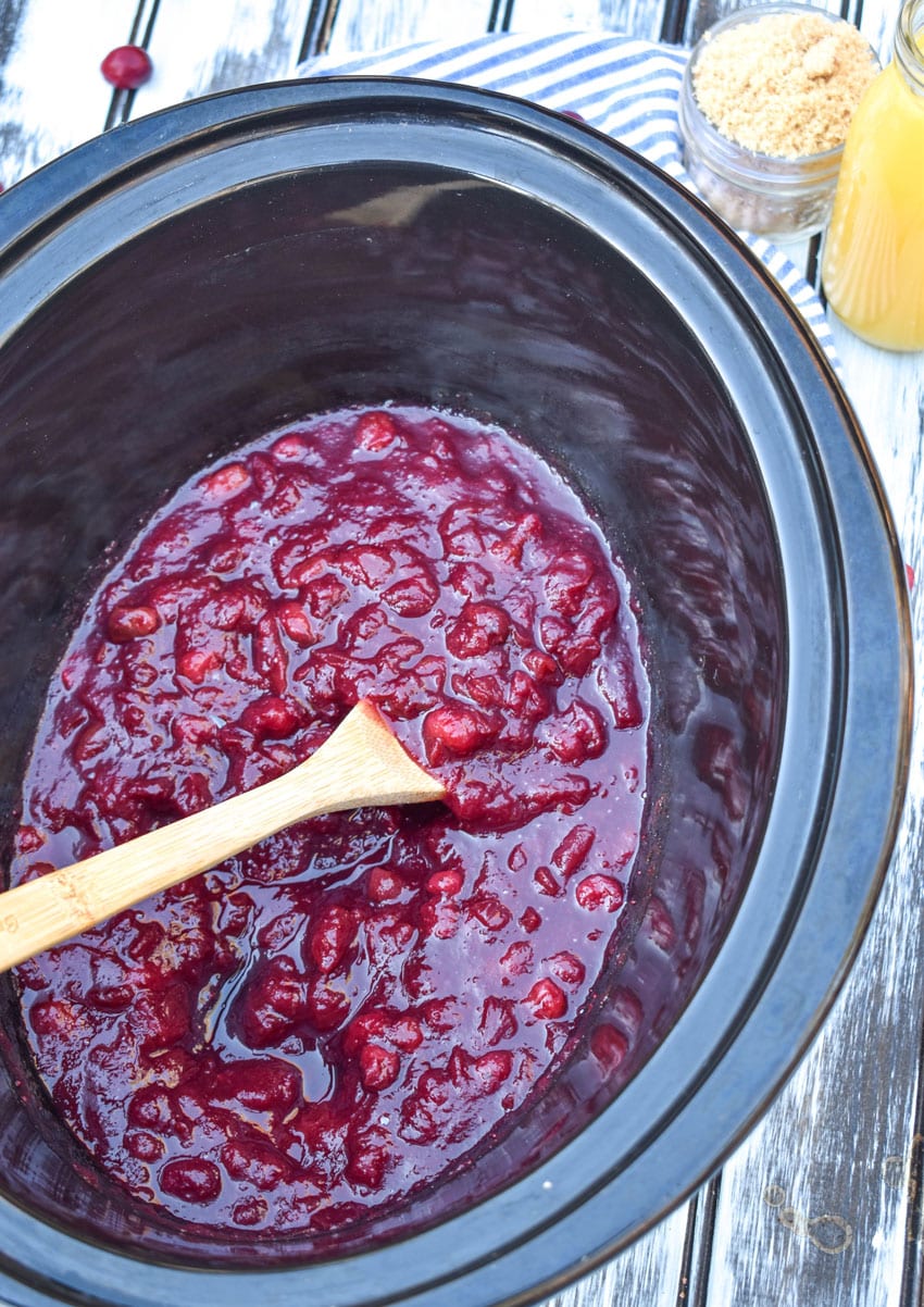 a wooden spoon stuck in a crockpot full of cranberry sauce