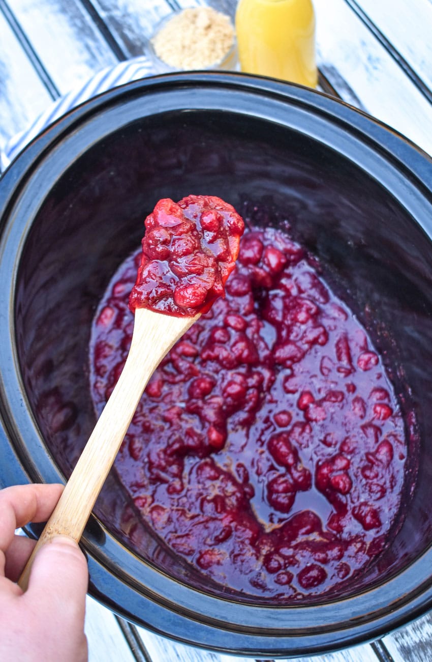 a wooden spoon holding up a scoop of crockpot cranberry sauce