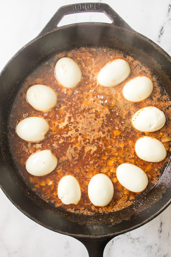hard boiled egg halves in butter sauce in a black skillet