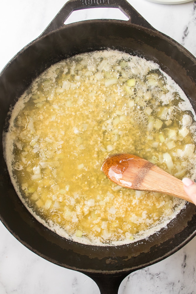 a wooden spoon in a skillet filled with melted butter and sauteed onions