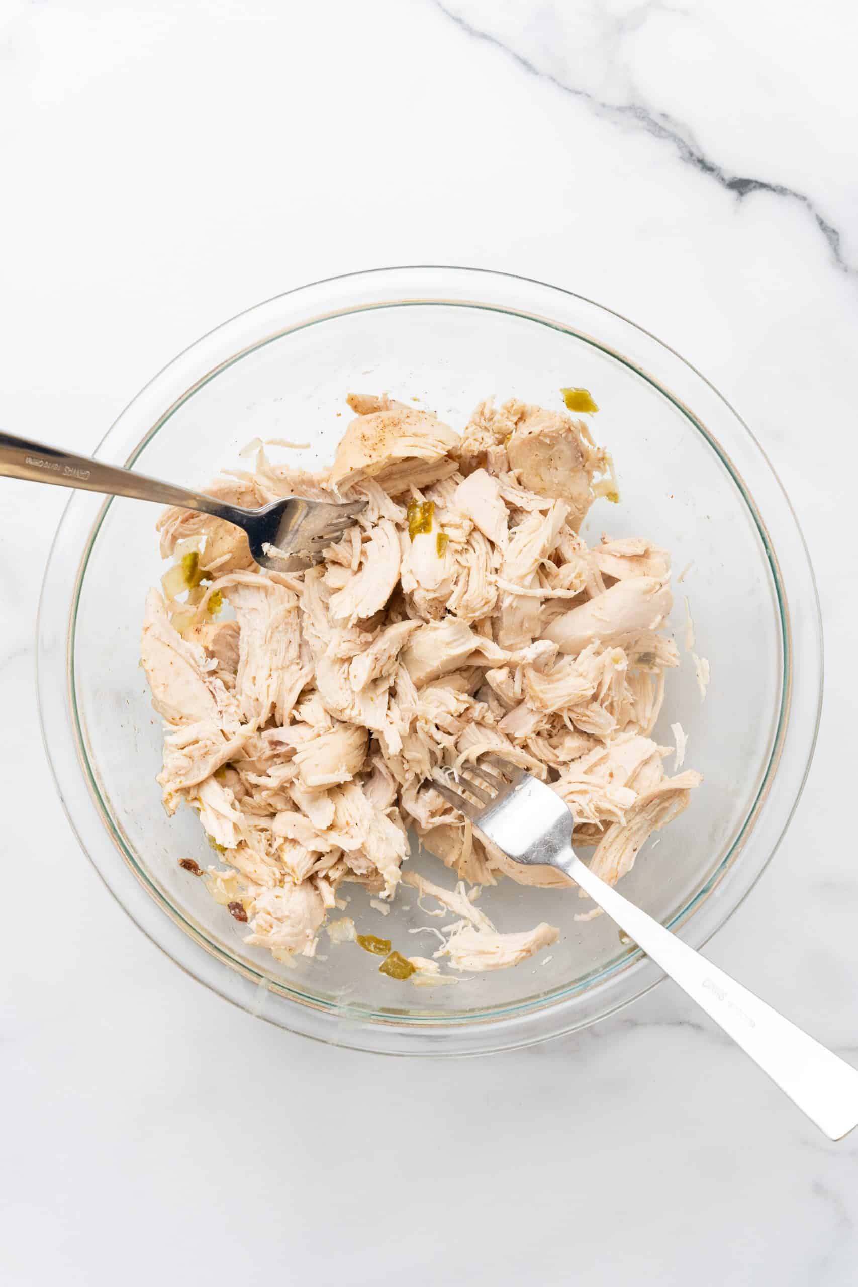 shredded chicken in a glass mixing bowl with two silver forks