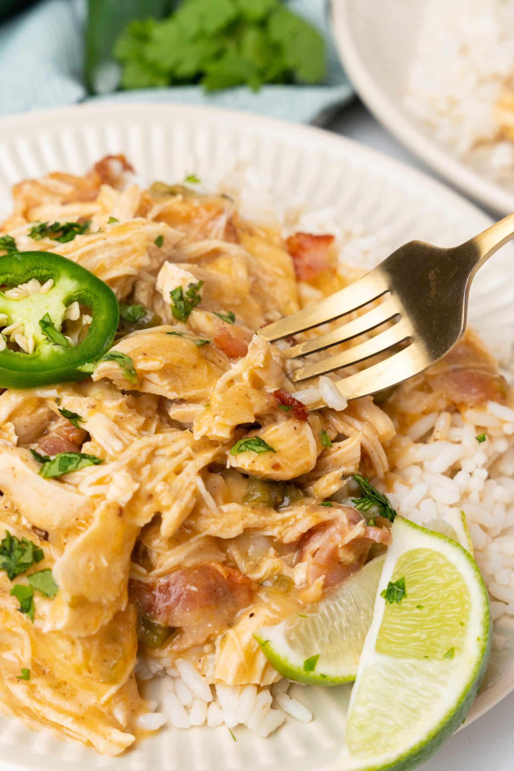 a gold fork digging into a plate of cheesy jalapeno chicken over steamed white rice