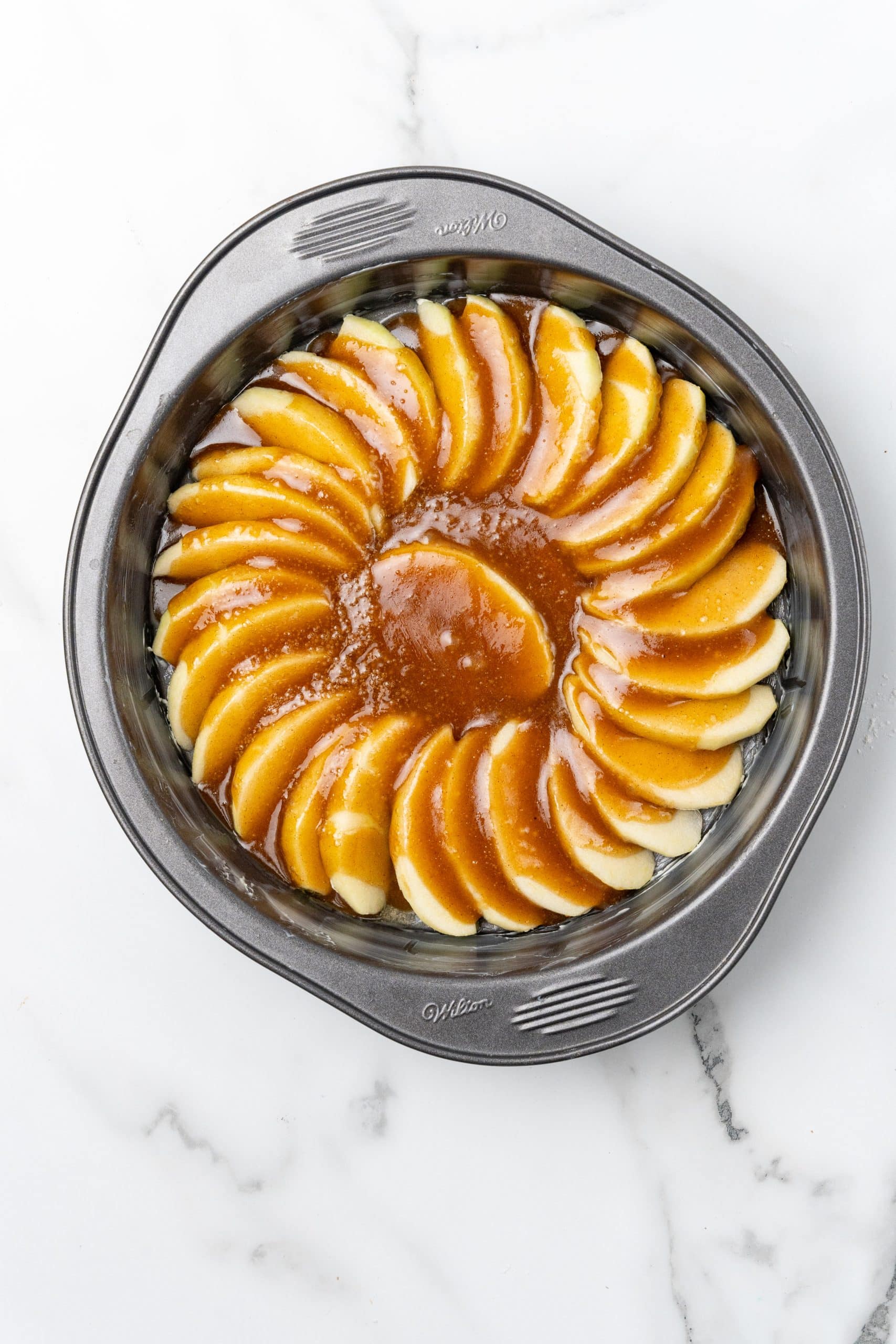 caramel sauce covered apple slices arranged in the bottom of a round cake pan