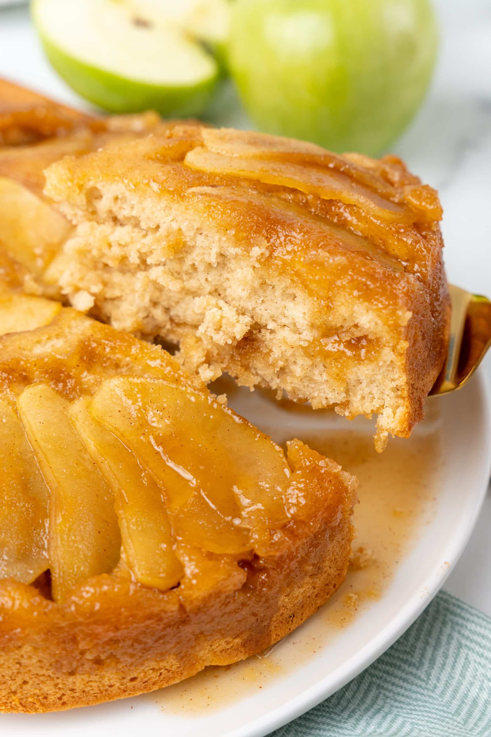 a slice of apple upside down cake being lifted off a white serving platter