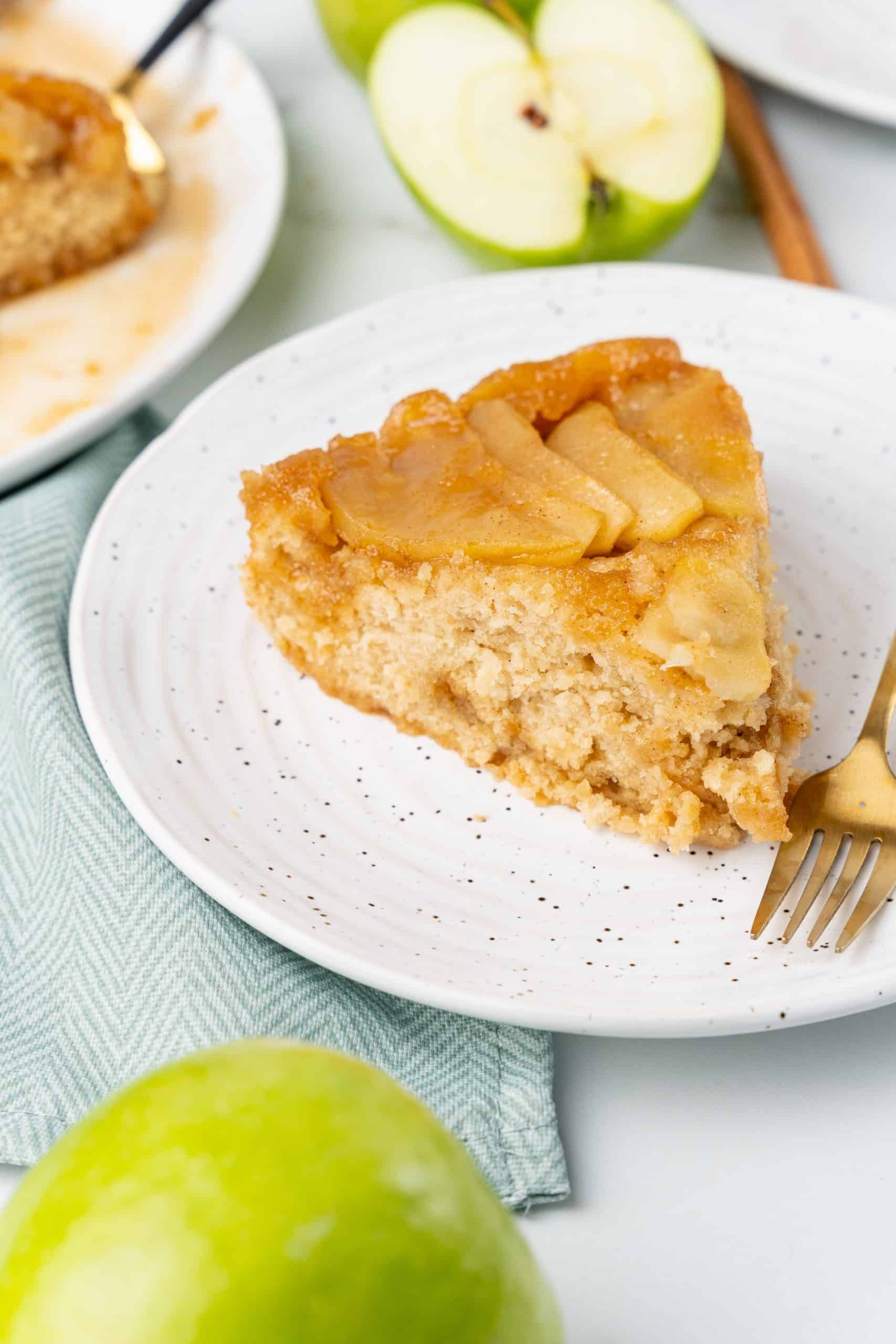 a slice of apple upside down cake on a white plate with a golden fork on the side