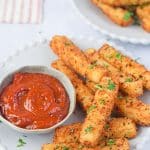 air fryer mozzarella sticks on a white plate with a small bowl of marinara sauce