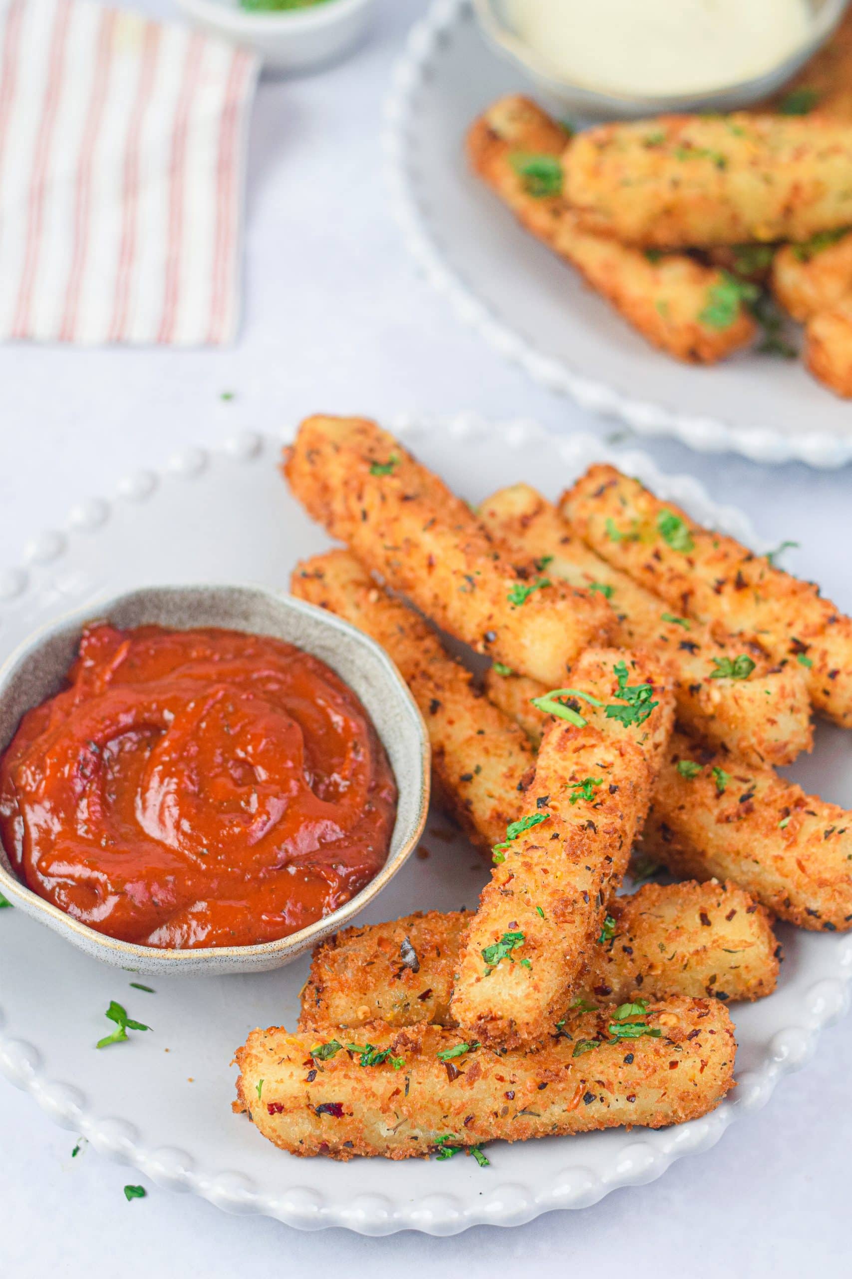 air fryer mozzarella sticks on a white plate with a small bowl of marinara sauce