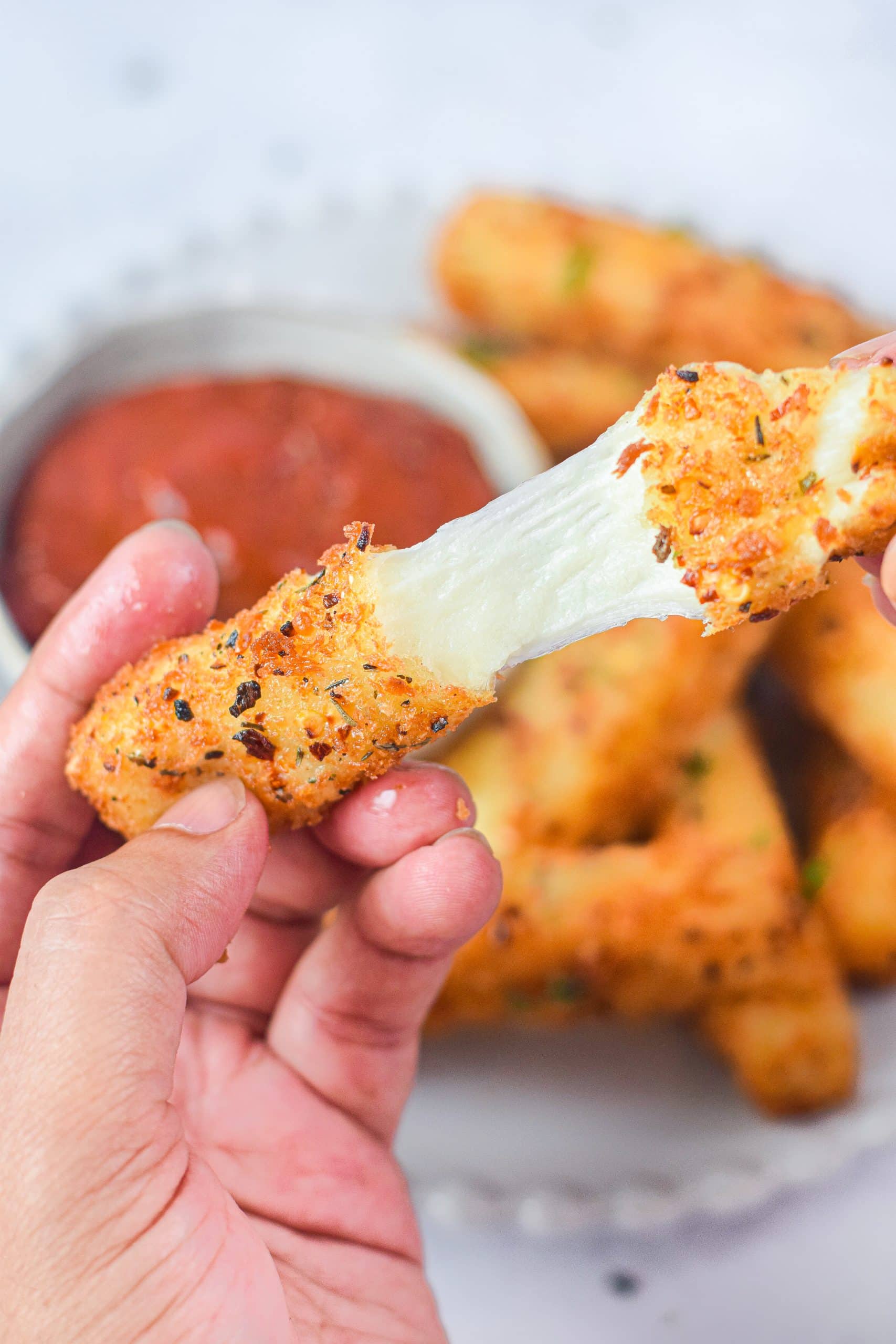a hand pulling apart an air fried mozzarella stick