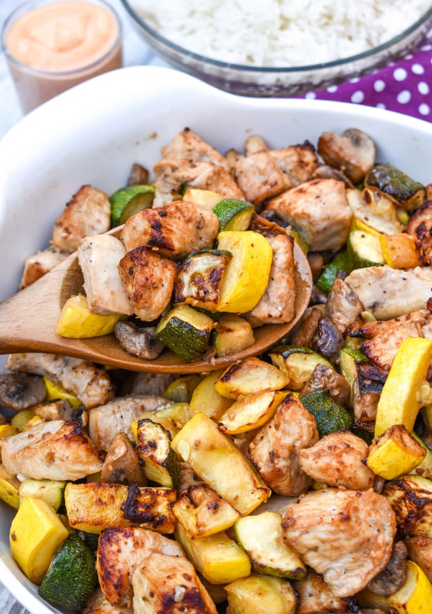 a wooden spoon scooping easy homemade hibachi chicken and vegetables out of a large white bowl