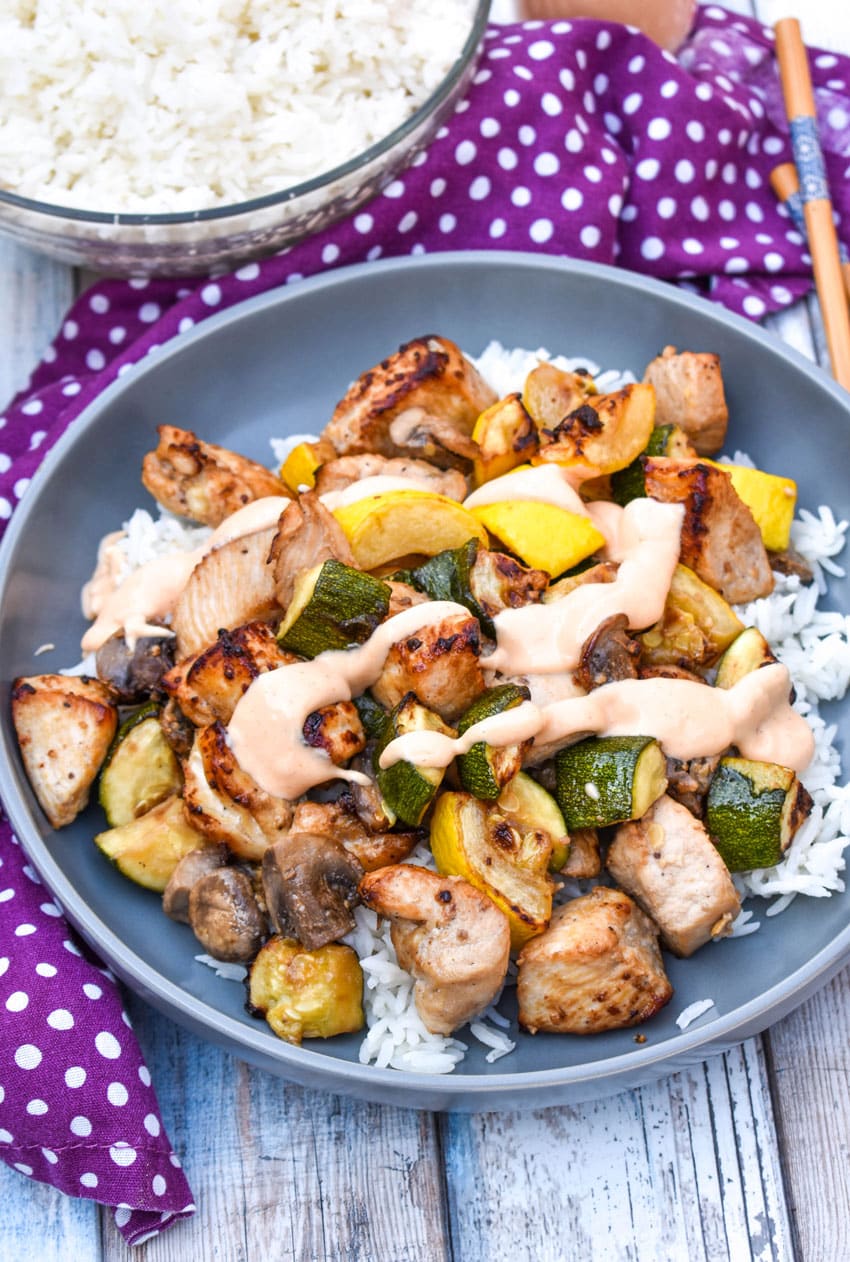 air fryer hibachi chicken and vegetables over steamed rice and topped with yum yum sauce on a gray plate