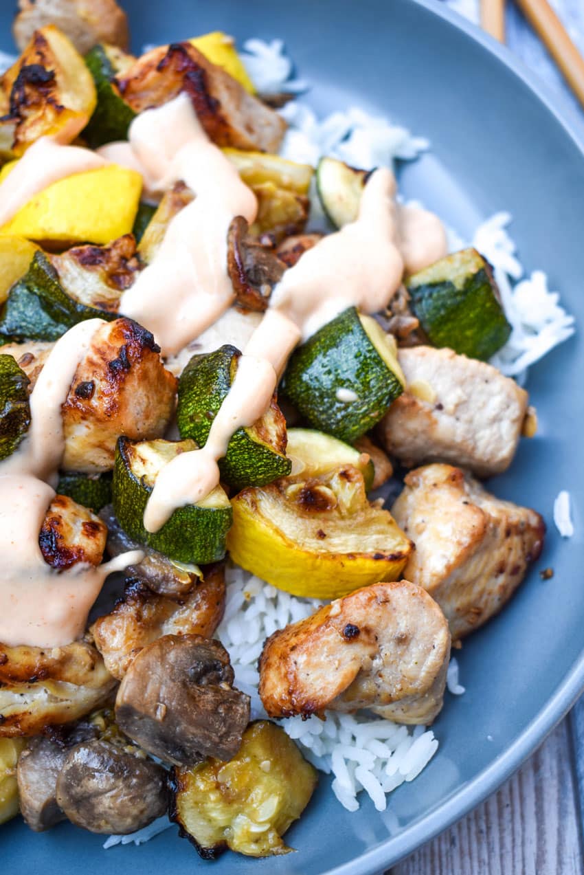 air fryer hibachi chicken and vegetables over steamed rice and topped with yum yum sauce on a gray plate