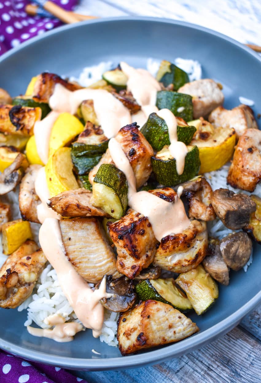 air fryer hibachi chicken and vegetables over steamed rice and topped with yum yum sauce on a gray plate