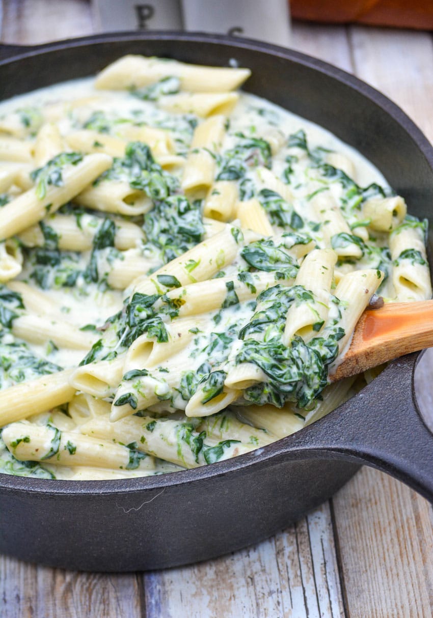a wooden spoon stuck in a cast iron skillet filled with creamed spinach mac and cheese