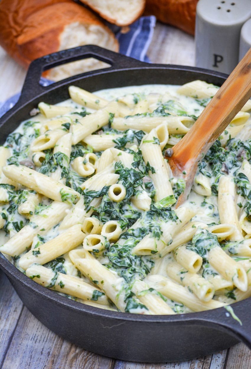 a wooden spoon stuck in a cast iron skillet filled with creamed spinach mac and cheese