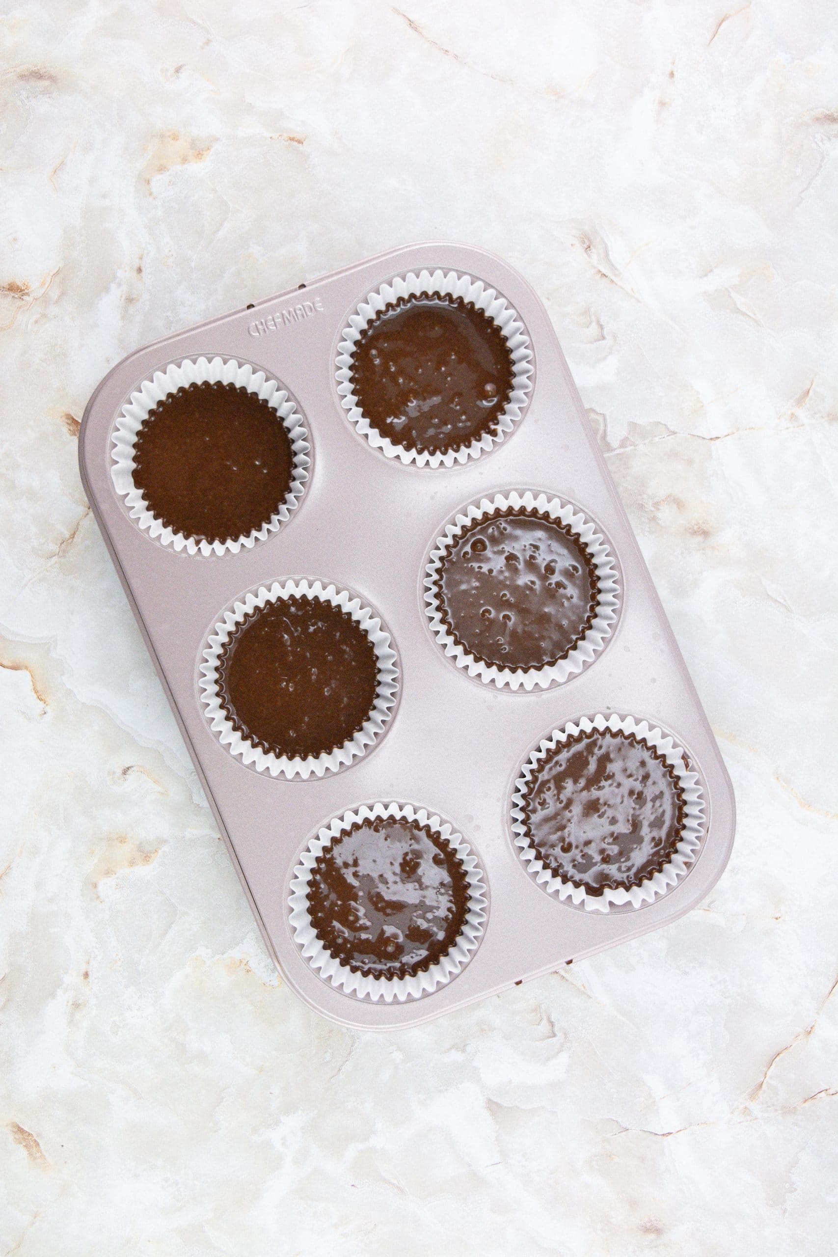 chocolate cupcake batter in white liners in a metal muffin tin