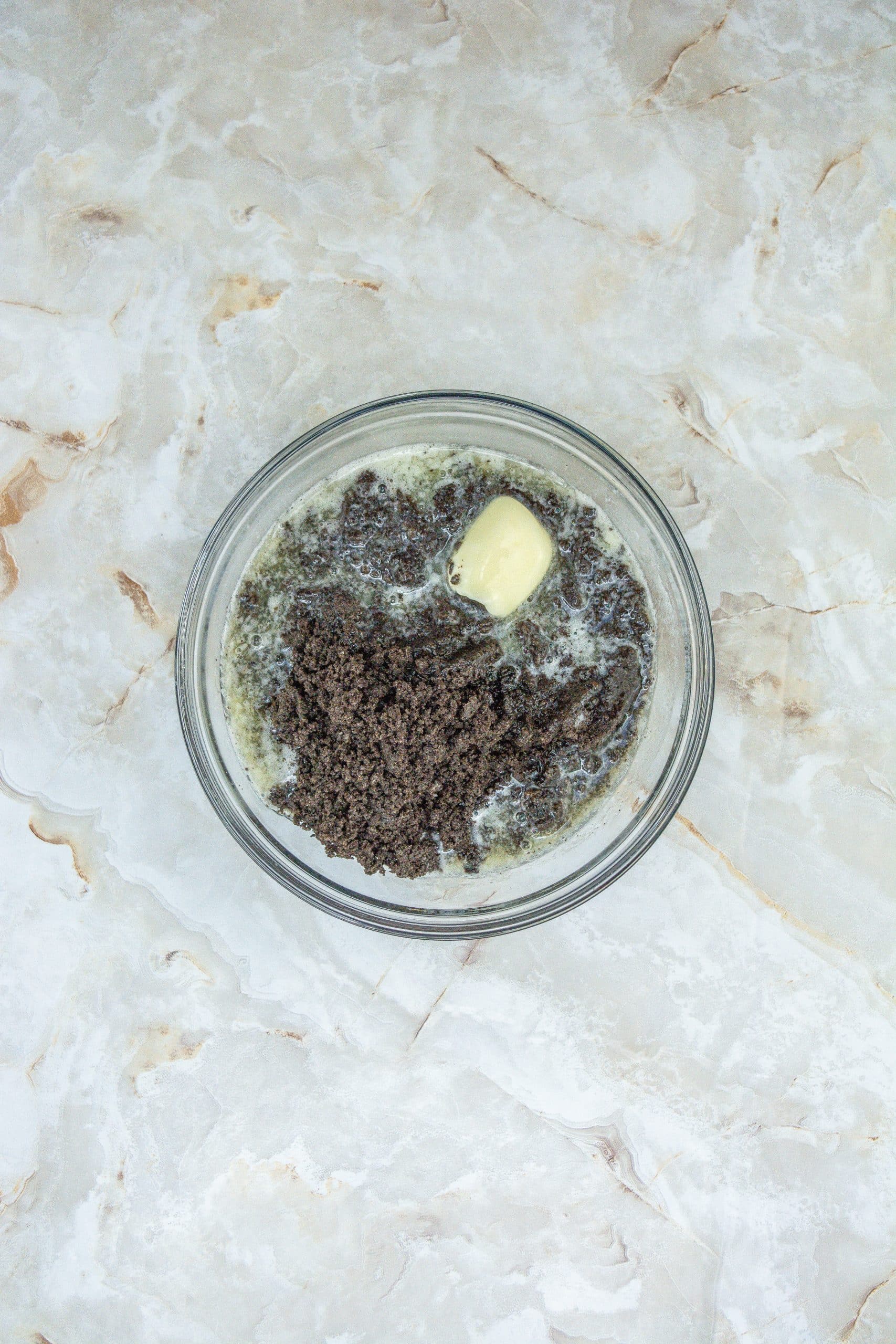 oreo crumbs and butter in a glass mixing bowl