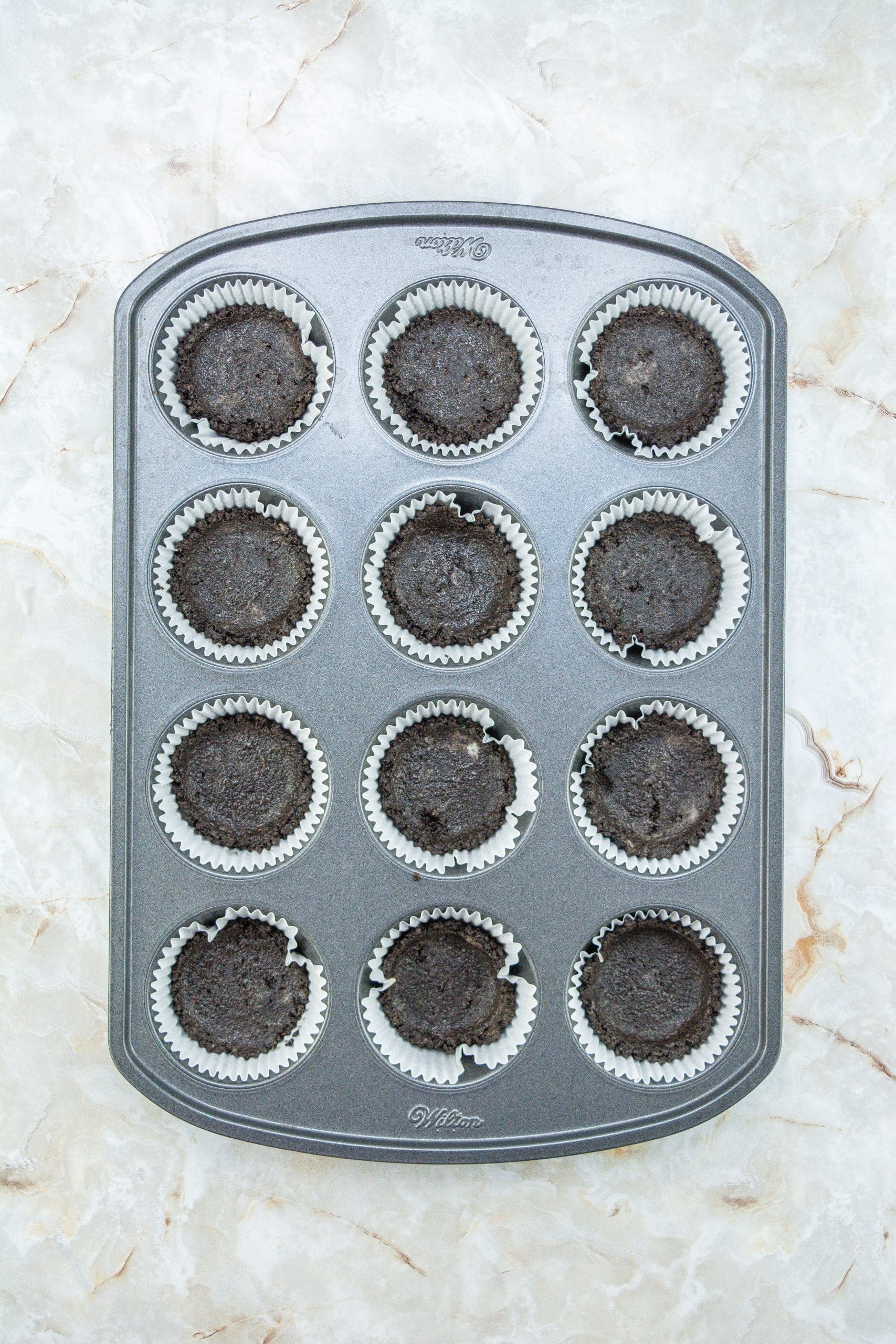 oreo crumb crust in cupcake liners in a metal pan