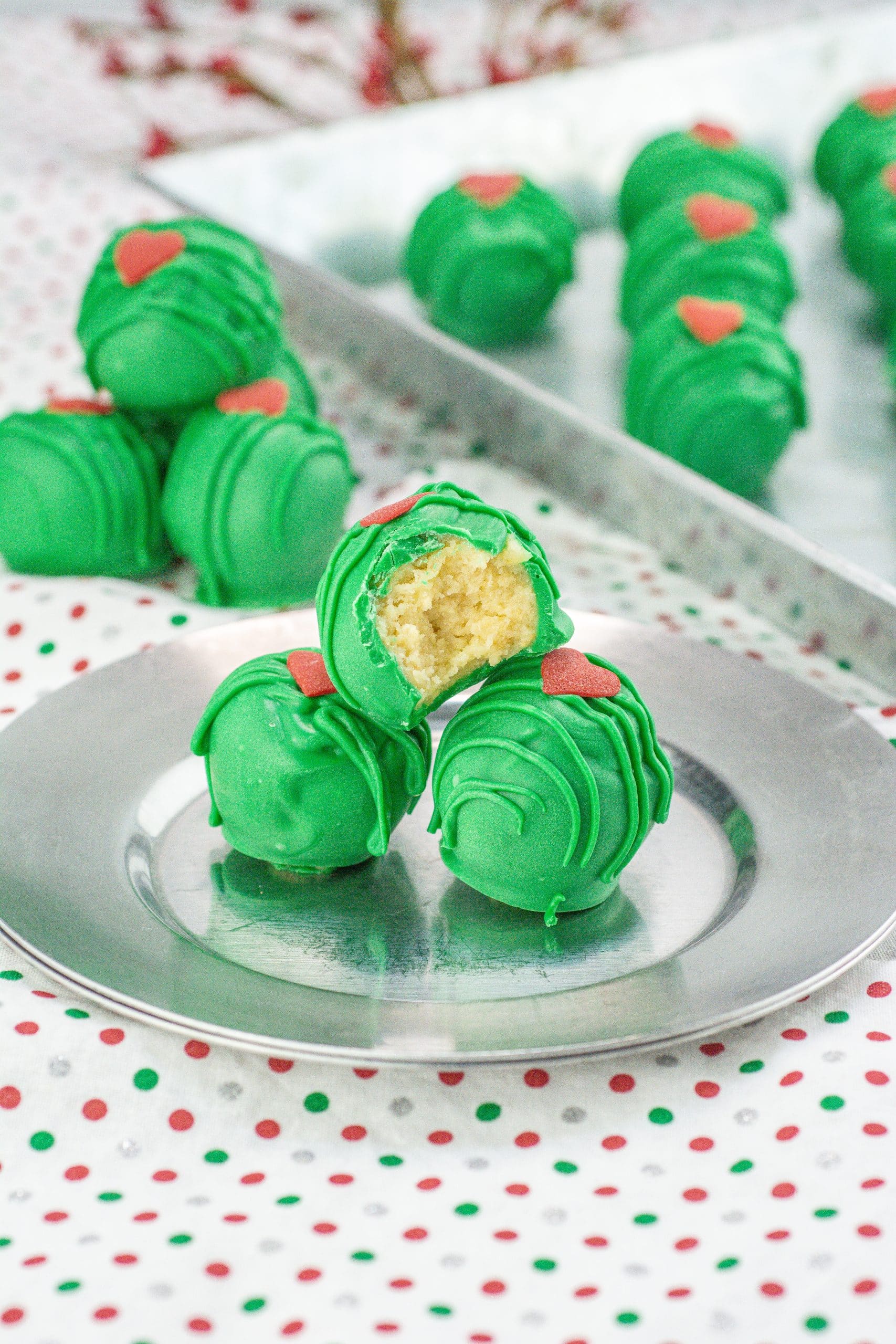 a bitten grinch cake ball on top of two other cake ball son a metal plate