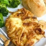 french onion pork chops on a white plate with steamed broccoli and a dinner roll on the side