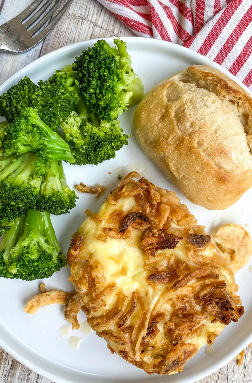french onion pork chops on a white plate with steamed broccoli and a dinner roll on the side