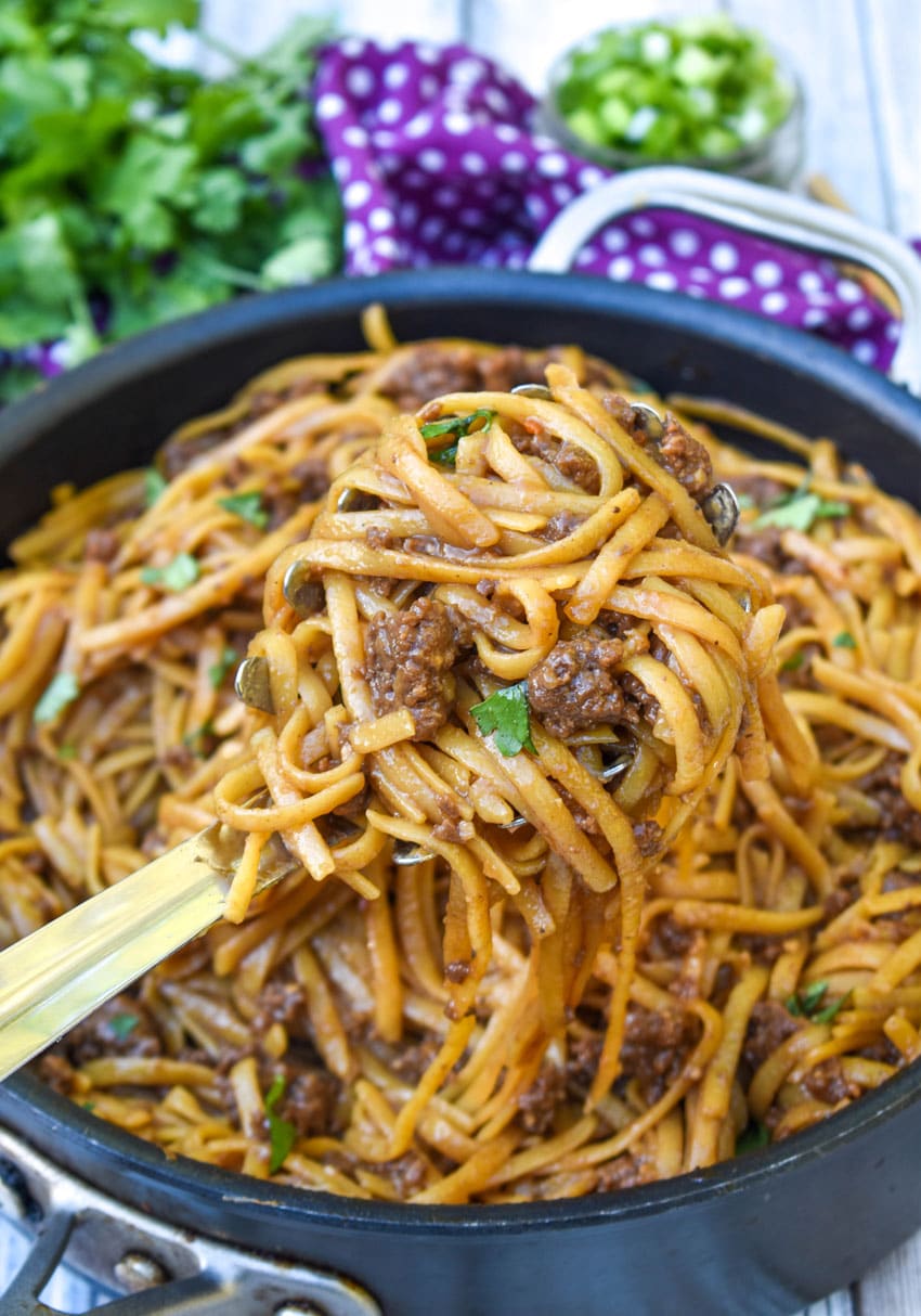 a silver spoon scooping mongolian ground beef and pasta out of a black skillet