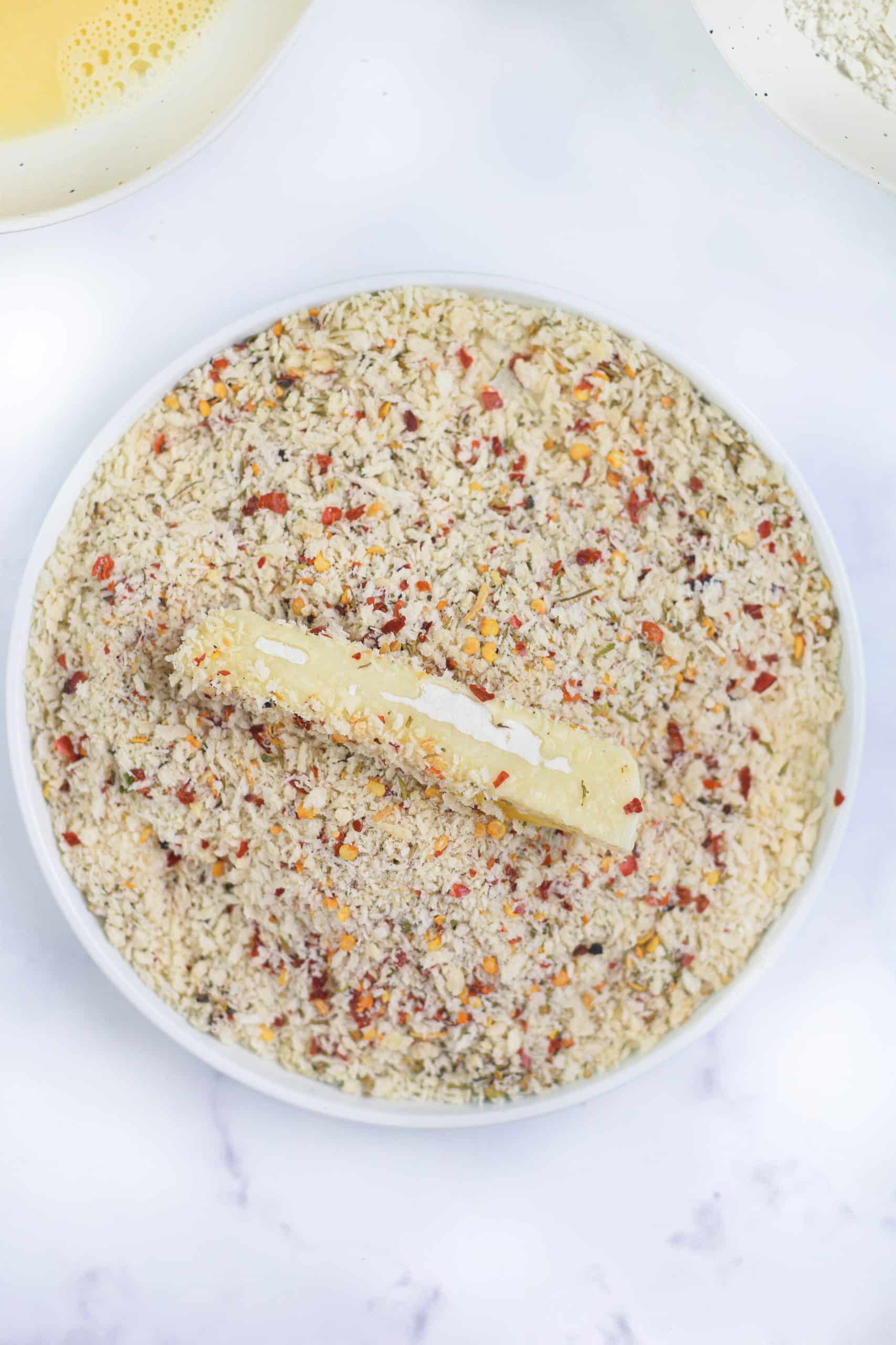 a piece of mozzarella cheese coated in seasoned panko bread crumbs on a white plate