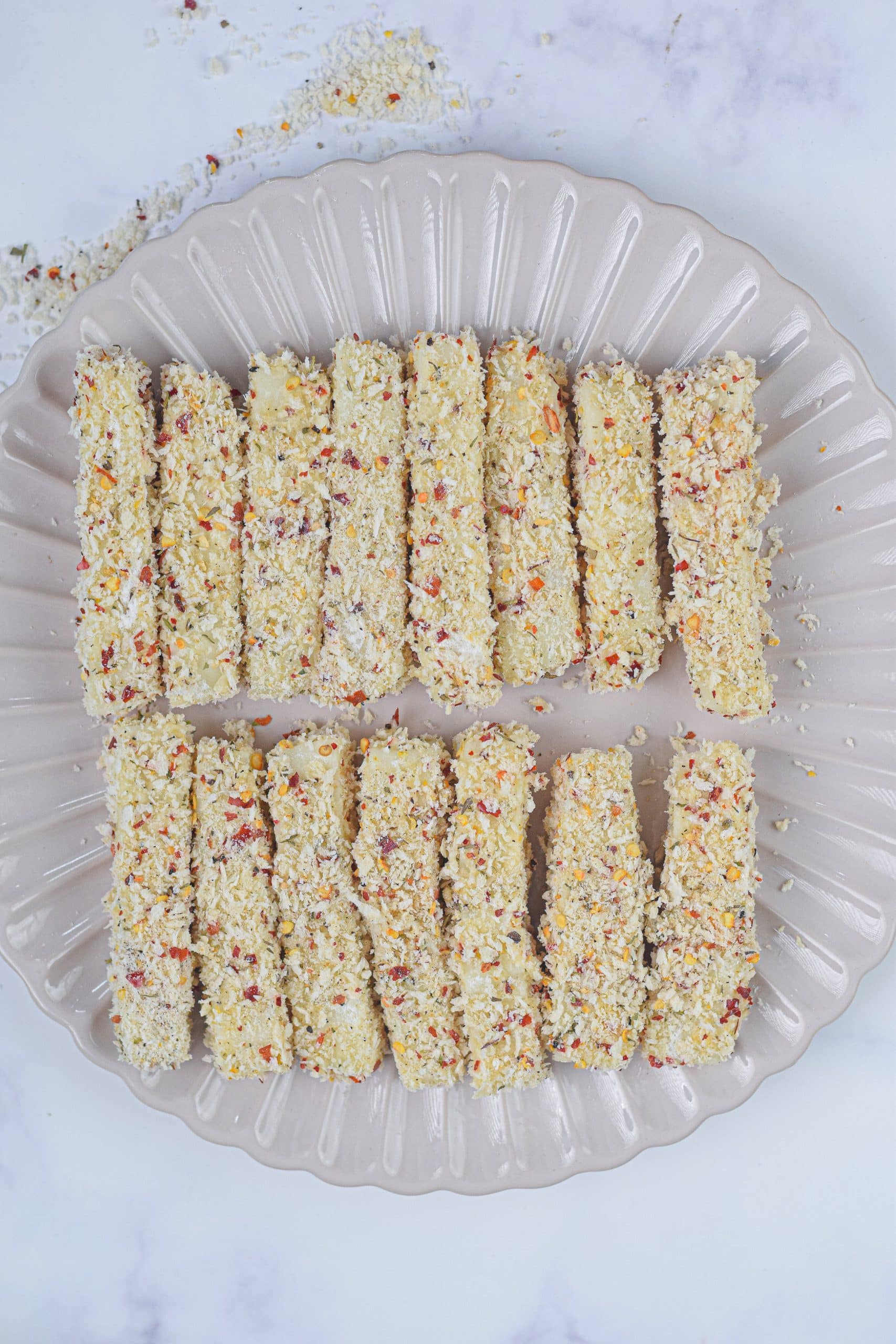 frozen breaded mozzarella sticks arranged in two rows on a white plate